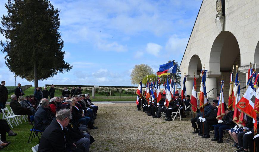 Cérémonie commémorative devant le mémorial, avec des porte-drapeaux alignés sous les arcades.
