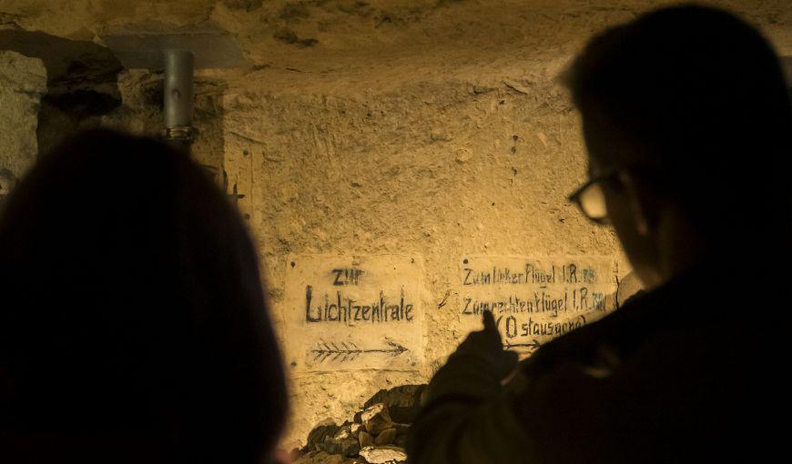 Personnes visitant une galerie souterraine où sont visibles d’anciennes inscriptions allemandes peintes sur la paroi calcaire.