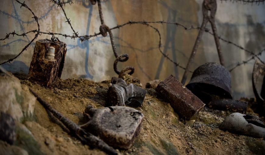Objets de guerre abandonnés dans la Caverne du Dragon, dont un casque militaire, des briques et des barbelés, disposés sur un sol terreux.