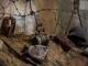 Objets de guerre abandonnés dans la Caverne du Dragon, dont un casque militaire, des briques et des barbelés, disposés sur un sol terreux.