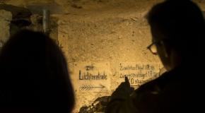 Personnes visitant une galerie souterraine où sont visibles d’anciennes inscriptions allemandes peintes sur la paroi calcaire.